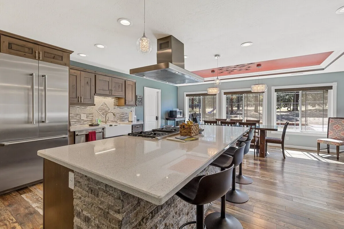 A spacious and modern kitchen with a large kitchen island, sleek stainless steel appliances, and an adjacent dining area bathed in natural light. The open layout emphasizes generous prep space and easy flow between the kitchen and dining areas, making it perfect for social cooking and group gatherings.