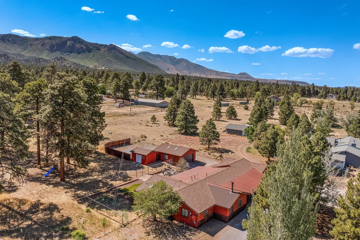 Red houses set against a backdrop of mountains and tall trees create a peaceful atmosphere. The environment suggests opportunities for hiking, outdoor gatherings, and family activities, with visible pathways leading into the woods.