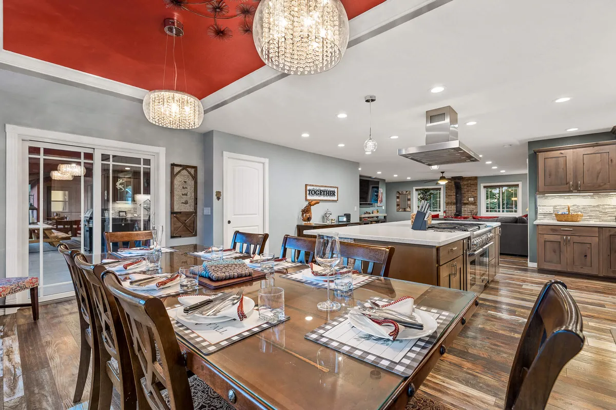 A warm and inviting dining area with a large table, elegant chandelier, and a kitchen island visible in the background. The open concept seamlessly connects the kitchen to the dining space, reinforcing the idea of togetherness during meal prep and dining.