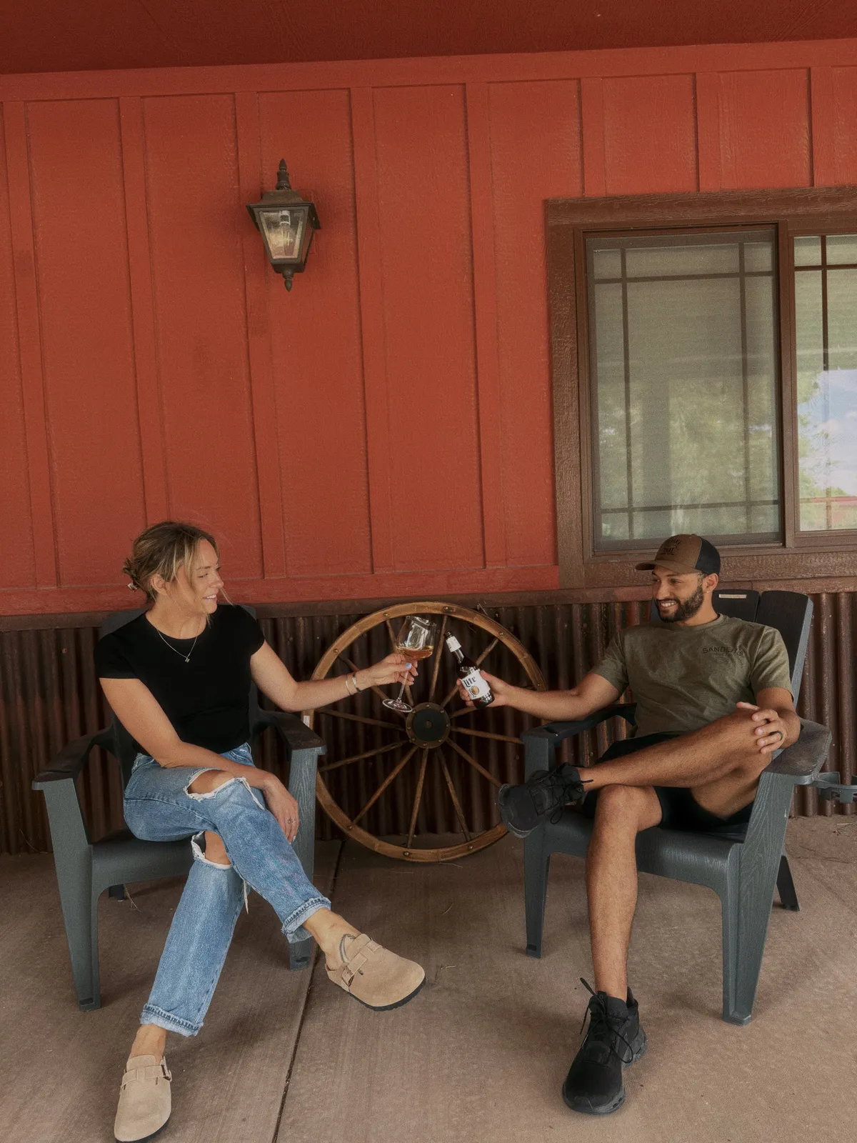 An exterior shot highlighting two people toasting drinks beside a rustic wall with a wagon wheel and outdoor seating area. The mood is friendly and celebratory, evoking moments of shared joy and memorable toasts.