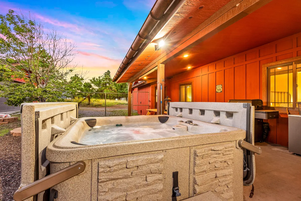 A bubbling hot tub sits on a wooden deck with evening lighting, inviting guests to relax and socialize. The setting offers views of the surrounding forest, creating a cozy and inviting atmosphere for group unwind sessions.
