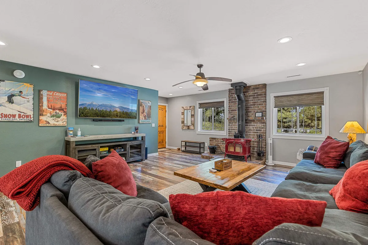 A spacious living room with a plush seating area centered around a brick fireplace. A large TV is positioned above the fireplace, with a wooden coffee table and comfortable couches creating a cozy, social atmosphere. Sunlight filters in, enhancing the welcoming mood.