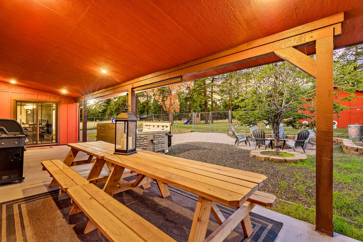 A welcoming outdoor dining space with a wooden picnic table, grill, lantern, and ample seating for groups. The setting hints at sunset, fostering an atmosphere of friendly gatherings, shared meals, and late-night conversations.