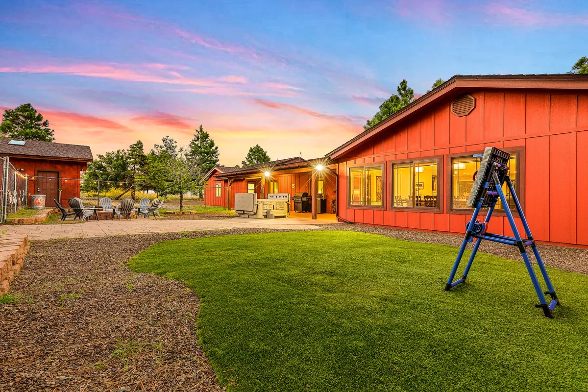 This exterior image showcases the red house with an outdoor seating area and a lush green lawn, set beneath a glowing sunset sky. The inviting fire pit area and expansive yard are clearly visible, suggesting spaces ideal for group gatherings, outdoor dining, and relaxation in nature.