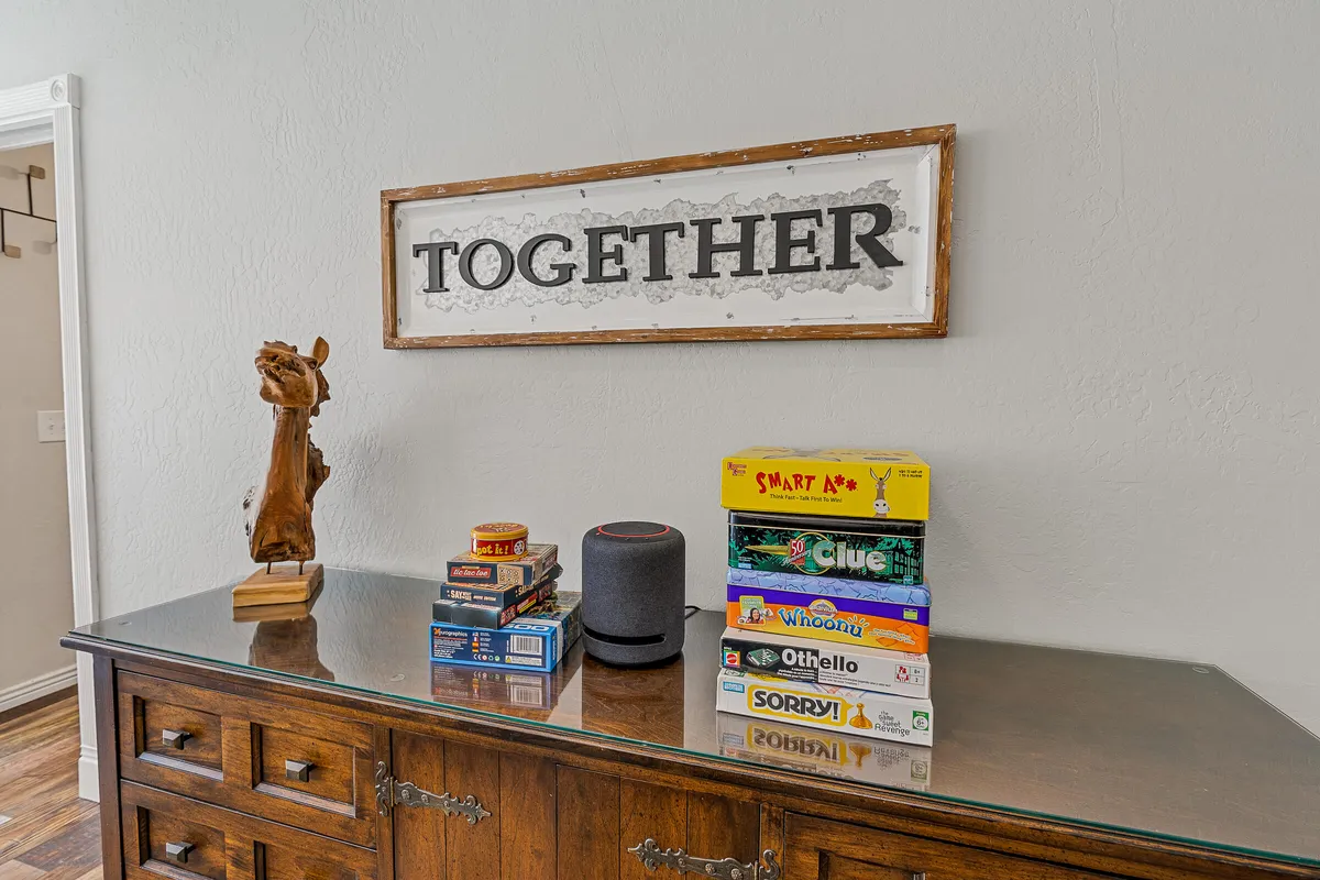 A cozy corner with a visible stack of board games, a smart speaker for music, and a framed sign, all atop a wooden cabinet. The atmosphere is warm and inviting, ideal for family board game nights and relaxed social gatherings.